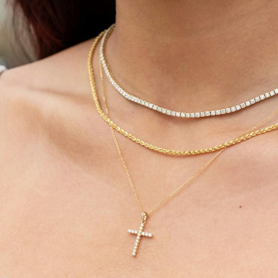 Layered necklaces featuring a diamond cross set in yellow gold, featured amongst a diamond line necklace in white gold and another diamond line necklace in yellow gold.