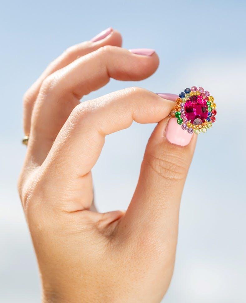 colorful gemstone ring being held in front of a background of the sky